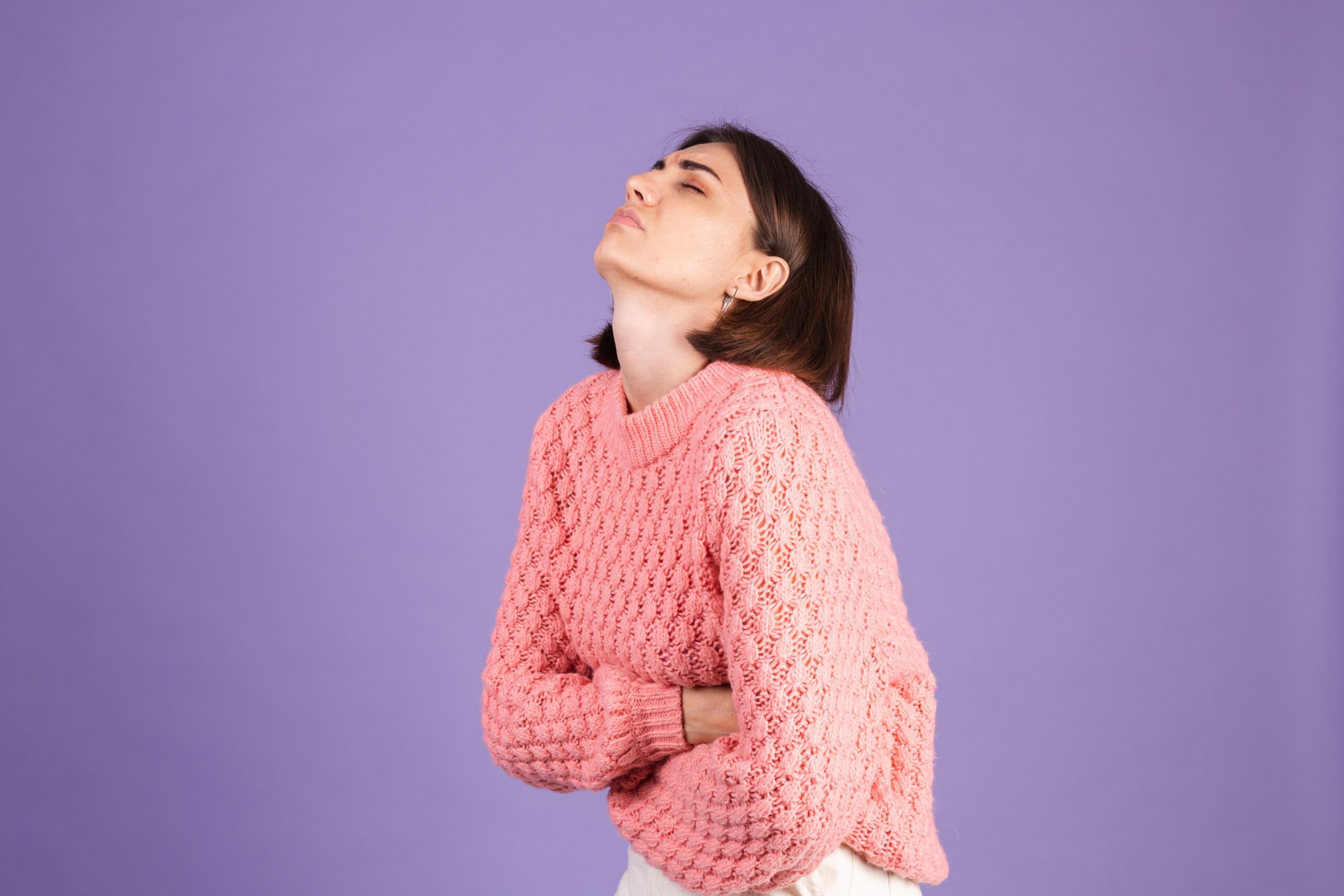 une femme avec un pull rose qui a très mal au ventre